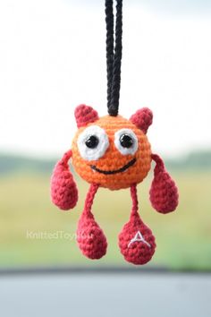 an orange crocheted toy hanging from a black cord with eyes and hands on it