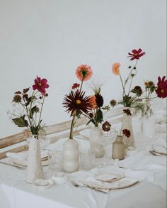 there are many vases with flowers in them on the dining room table set for dinner