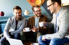 three men sitting on a couch drinking coffee and looking at a laptop - stock photo - images