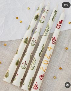 three white candles decorated with gold and red decorations on top of a cloth covered table