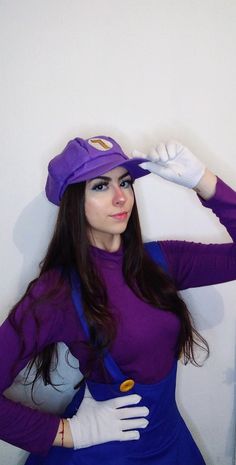 a woman in a purple dress and hat poses for the camera with her hands on her head