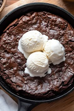 two scoops of ice cream sit on top of a chocolate cake in a cast iron skillet