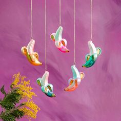 four colorful birds hanging from strings in front of a purple wall with yellow flowers on it