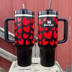 two travel mugs sitting on top of a wooden table next to a red barn