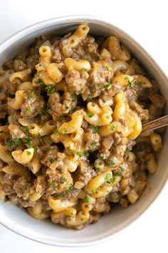 a close up of a bowl of food with pasta and meat in it on a table