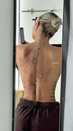 a woman with tattoos on her back looking at herself in the mirror and holding a cell phone