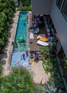 an aerial view of people swimming in a pool surrounded by greenery and trees on the side of a building