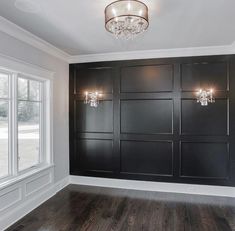 an empty room with black paneling and chandelier