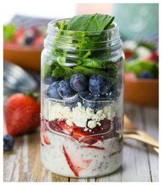 a mason jar filled with yogurt, berries and spinach on top of a wooden table