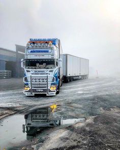 a semi truck driving down a road next to a large building on a foggy day