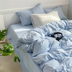 an unmade bed with blue sheets and headphones on the bottom shelf next to a potted plant