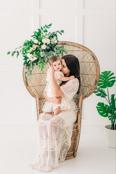 a mother and her daughter sitting on a wicker chair in front of a plant