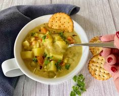 a person holding a spoon over a bowl of soup with crackers on the side