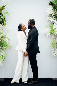 a man and woman standing next to each other in front of a wall with flowers