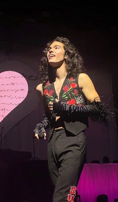 a woman standing on top of a stage wearing black pants and a cropped shirt