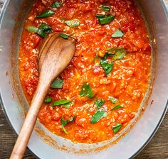 a wooden spoon in a pot filled with tomato sauce and basil leaves on the side