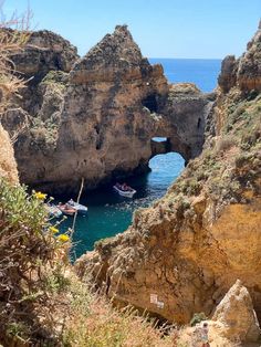 two small boats are in the water near some rocks and cliffs with an arch on one side