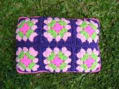 a crocheted pillow is laying on the grass with pink, green and purple flowers