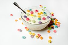 a bowl filled with cereal sitting on top of a white table next to lots of colorful cereal