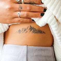 a woman with tattoos on her stomach and hands behind her back, showing the mountain tattoo