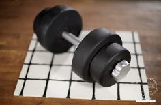 two black dumbbells sitting on top of a white and black checkered mat