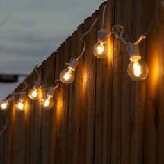 some lights are hanging on the side of a wooden fence with snow in the background