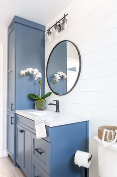 a bathroom with blue cabinetry and white flowers in a vase on the sink counter