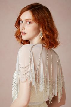 a woman with red hair wearing a white dress and pearls on her shoulders, standing in front of a pink background