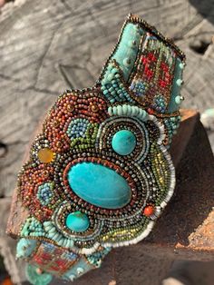 This beautiful bead embroidered cuff features a large genuine turquoise cabochon at the center, flanked by 2 smaller turquoise cabochons on either side.  The beadwork surrounding the cabochons is worked in a style that emulates the beautiful floral beadwork of the Ojibwe tribes of the Pacific Northwest.  All beads are hand stitched (2 beads at a time) into a felt foundation, and backed by ultrasuede.  Flanking each side of the cuff are 2 pieces of loomed beadwork in a pattern that I designed to compliment the center beadwork.  These are mounted on a beautiful sturdy piece of 2-tone taffeta that is beaded with aged turquoise glass beads from Portugal.  The closure of this cuff incorporates a lovely turquoise colored glass button from the Czech Republic and a deerskin thong that loops around Elegant Turquoise Beaded Gems And Cabochons, Artisan Turquoise Cuff Bracelet For Festivals, Unique Handmade Turquoise Beads, Gems And Cabochons, Artisan Turquoise Beaded Bracelet, Artisan Hand-stitched Festival Jewelry, Handmade Turquoise Artisan Cuff Bracelet, Handmade Artisan Turquoise Cuff Bracelet, Handmade Artisan Turquoise Beads, Adjustable Bohemian Cuff Bracelet With Cabochon