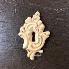 an ornately carved light switch plate on a dark wood surface, with the letter i in