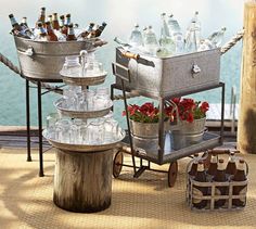 three metal containers filled with bottles on top of a wooden table next to water and flowers