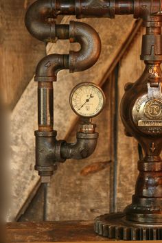 an old fashioned steam clock on top of a wooden table next to pipes and gauges