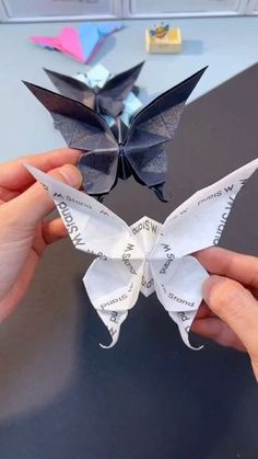 two hands holding origami butterflies on top of a black table in an office