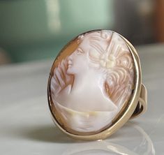 Cameo ring, wonderful vintage hand carved hard-stone portrait cameo ring. This cameo has lovely details like her tiny orange blossom hair ornament and lace collar which frame this enchanting expertly carved portrait cameo. A really neat old piece! The cameo is in very good condition, increasingly hard to find. Ring has a luxurious weight of 5.1 grams! Currently the band is a size US 5 3/4 and could be sized by my local jeweler for an additional small fee if desired by adding custom sizing to your cart upon checkout here: https://www.etsy.com/listing/187585008/ring-sizing-for-white-or-yellow-gold Total ring weight is a luxurious 5.1 grams. No longer stamped inside of band due to sizing at some point in history, tested/guaranteed solid 14K gold. If you would like to view additional vintage a Antique Cameo Ring Collectible, Vintage Cameo Signet Ring, Vintage Cameo Rings For Wedding, Elegant Wedding Cameo Signet Ring, Vintage Cameo Ring With Oval Cabochon, Vintage Cameo Oval Cabochon Rings, Antique Cameo Signet Ring For Weddings, Antique Cameo Signet Ring Collectible, Elegant Oval Cameo Engraved Ring