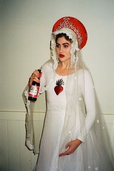 a woman dressed as a bride holding a bottle of booze and wearing a red hat