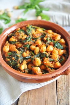 a brown bowl filled with chickpeas and spinach on top of a wooden table