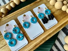 three pairs of blue and black earrings sitting on top of a wooden table next to beads