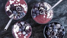 three bowls filled with blueberries and other fruit on top of a table next to spoons