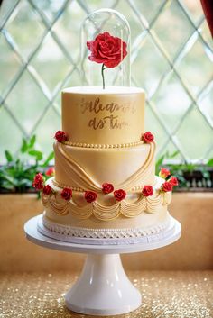 a three tiered cake with a red rose on top is sitting in front of a window