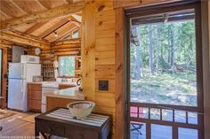 a kitchen and living room in a cabin with wooden walls, windows, and wood flooring