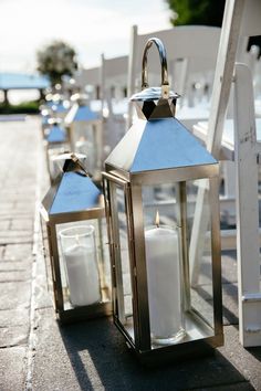 two white lanterns sitting next to each other on top of a stone walkway with chairs in the background