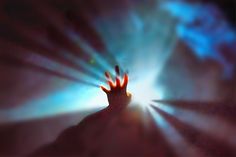 a person's hand reaching up into the air with light coming from behind them