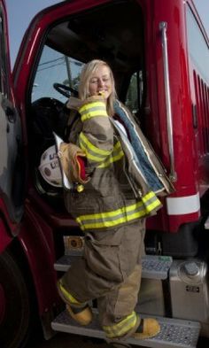 a woman in firefighter gear standing next to a red truck with the door open