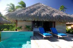 two chaise lounge chairs next to an outdoor swimming pool with thatched roof over it