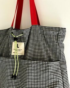 a black and white checkered tote bag hanging on a wall with a red handle