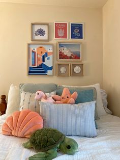 stuffed animals and pillows on a bed in a room with pictures above it, along with an ocean themed pillow