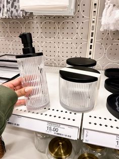 a person is holding a glass bottle in front of some other items on a shelf