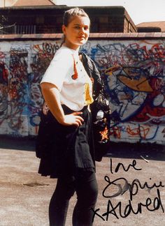 a woman standing in front of a graffiti covered wall with her hands on her hips