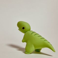 a green plastic toy dinosaur on a white surface with its head turned to the side