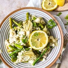 a white plate topped with chicken and asparagus next to lemon wedges on a table